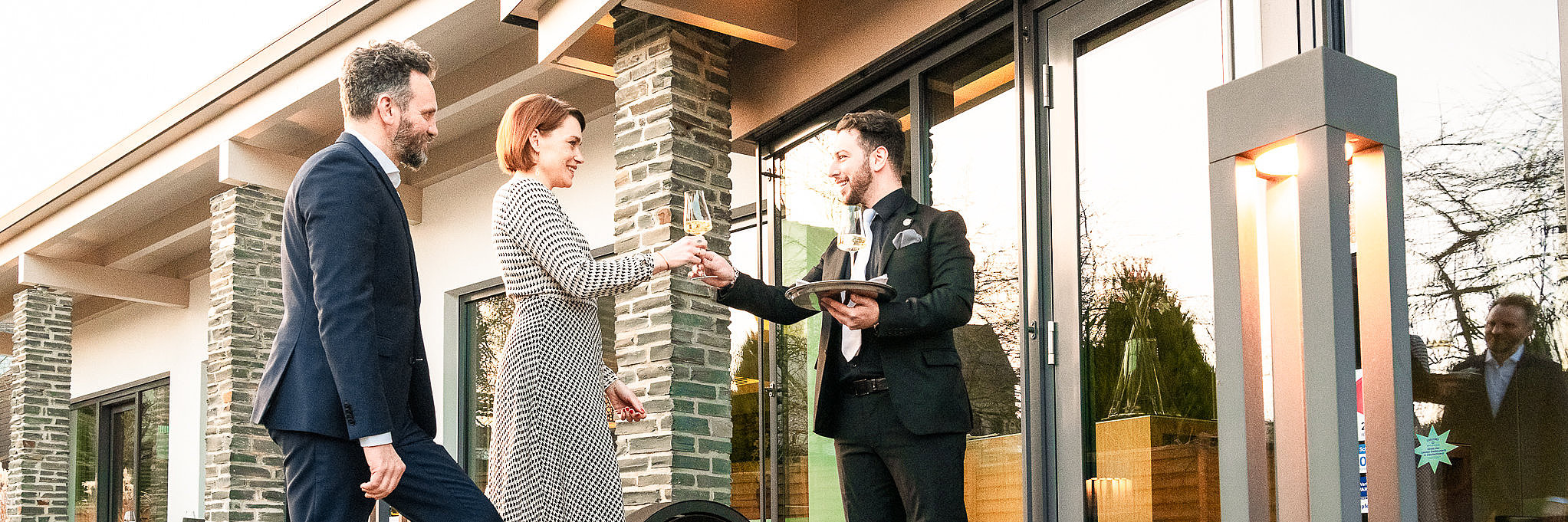 Personen besuchen Restaurant Das Foto zeigt zwei Personen, die von einem Kellner begrüßt werden. Sie besuchen ein Gourmetrestaurant und erhalten gerade ein Glas Wein.