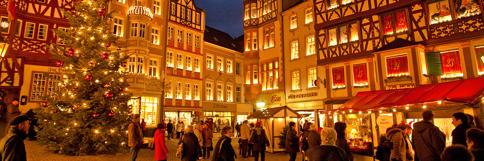 Das Bild zeigt den weihnachtlichen Marktplatz von Bernkastel bei Nacht mit Weihnachtsmarktständen und Tannenbaum.